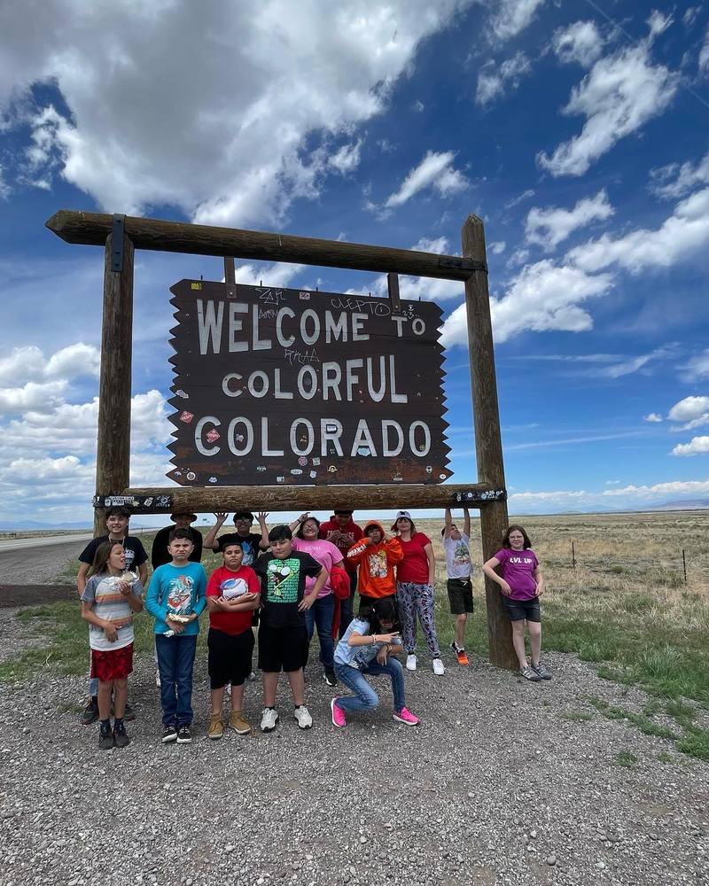 Students standing in front of the Welcome to Colorado sign